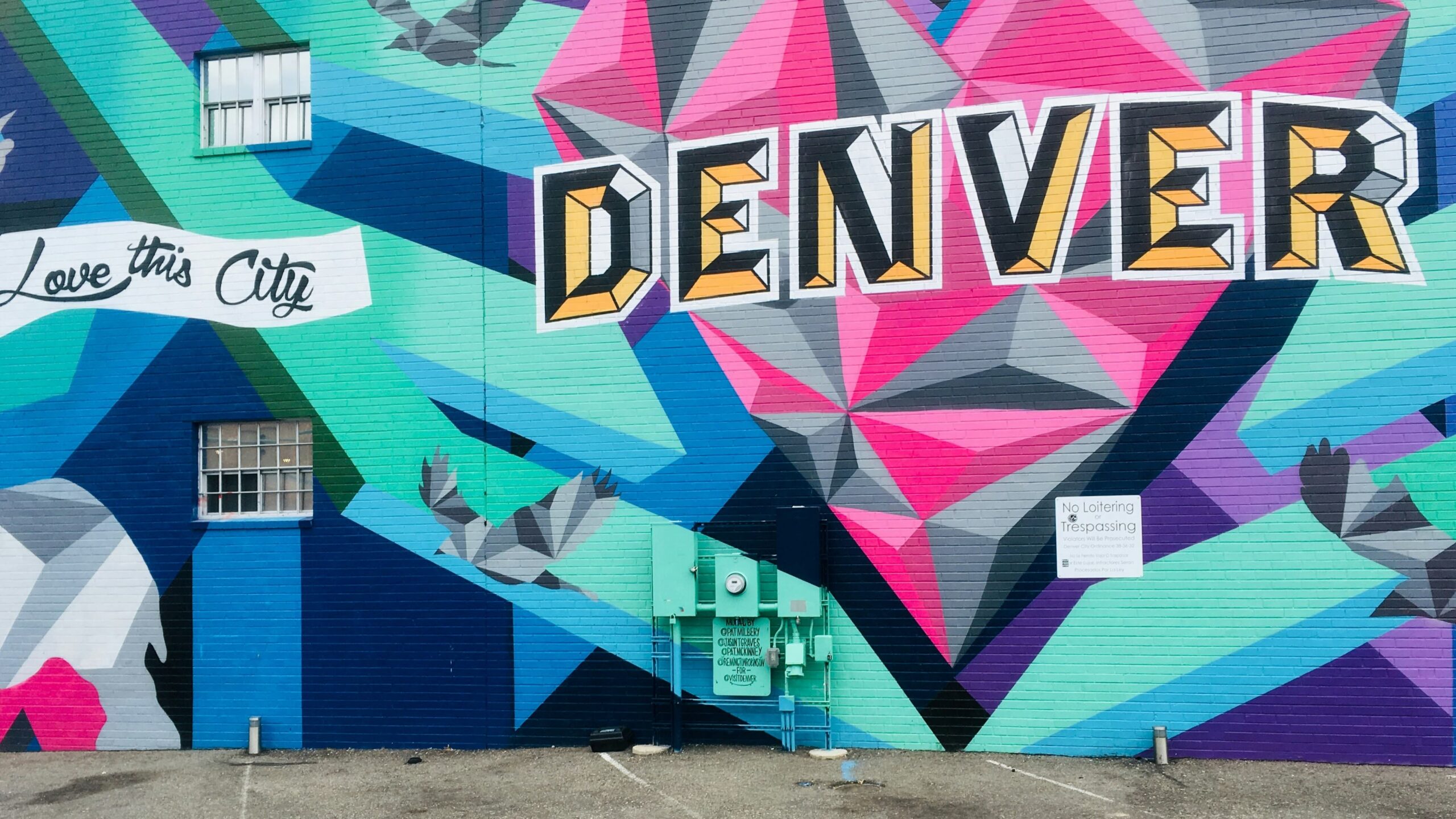 Colorful mural with bold geometric shapes in blue, pink, and green. The words "DENVER" and "Love this City" are prominently displayed, creating a lively and vibrant atmosphere.