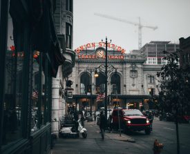 Foggy urban street scene featuring a grand Union Station with a glowing neon sign. Red truck and scooter in foreground, cranes visible above.